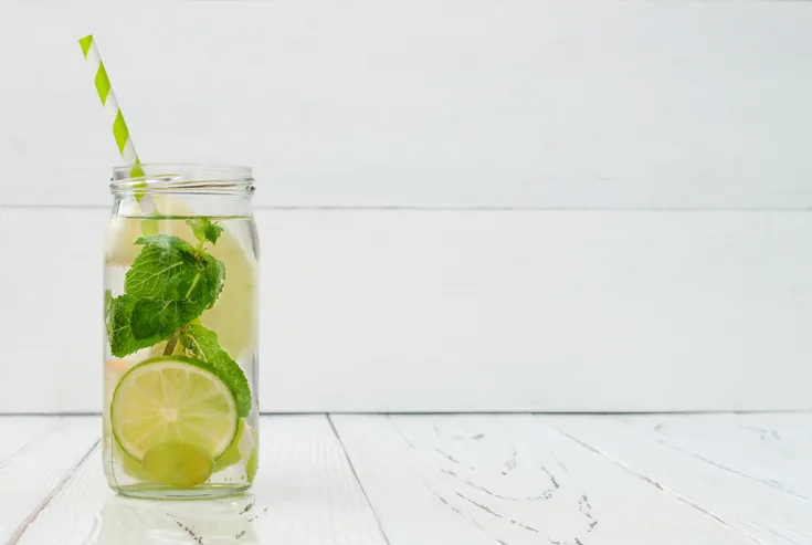 Glas mit Limette, Minze und grün-weiß gestreiften Strohhalm