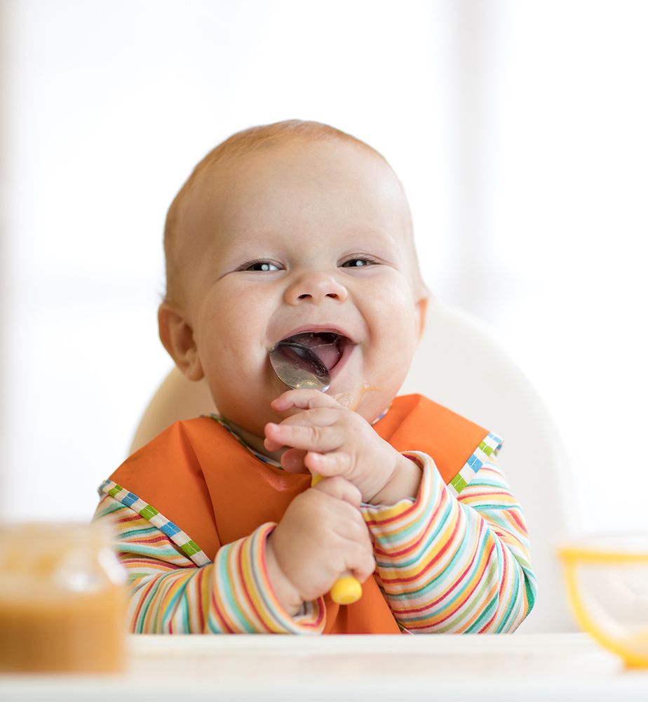 Baby mit Löffel im Mund lächelt in die Kamera