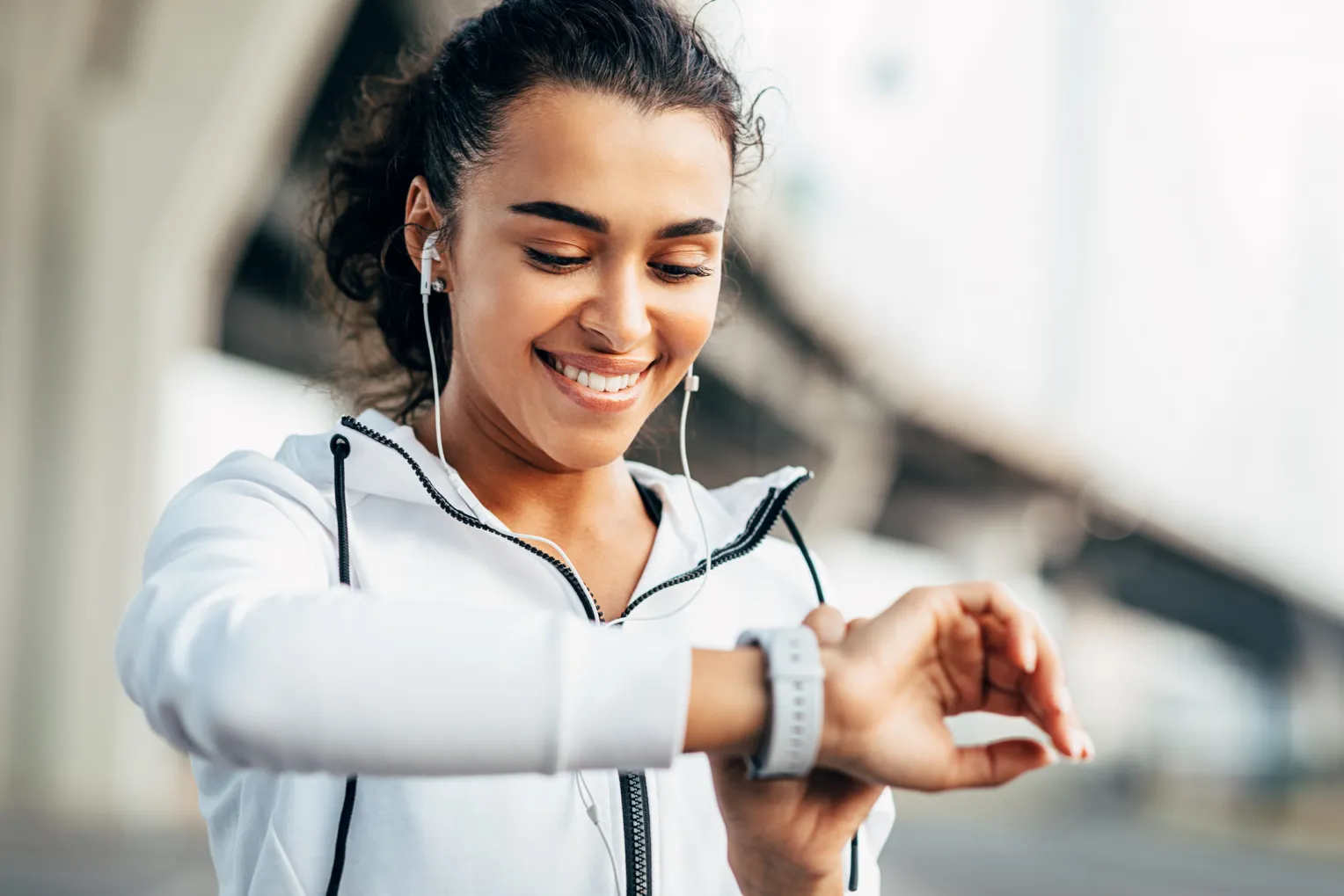 Sportlich gekleidete Frau mit Kopfhörern schaut lächelnd auf ihre Smartwatch.