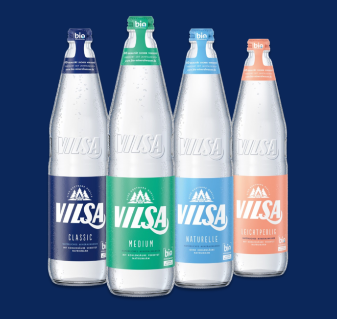 Vier Glasflaschen von VILSA Bio-Mineralwasser stehen nebeneinander. Die linke Flasche ist VILSA Classic mit Kohlensäure, die mittlere ist VILSA Medium mit weniger Kohlensäure, die rechte ist VILSA Naturelle ohne Kohlensäure und die letzte Flasche ist VILSA Leichtperlig.