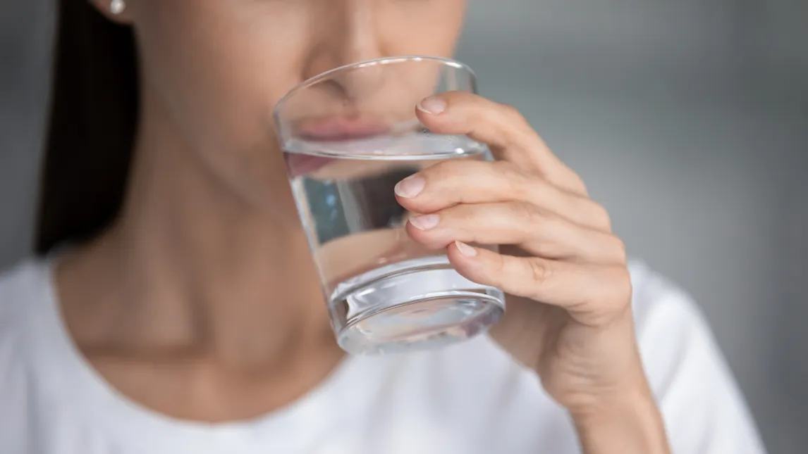 Nahaufnahme einer Frau, die ein Glas klares Wasser an den Lippen hält, bereit zu trinken.