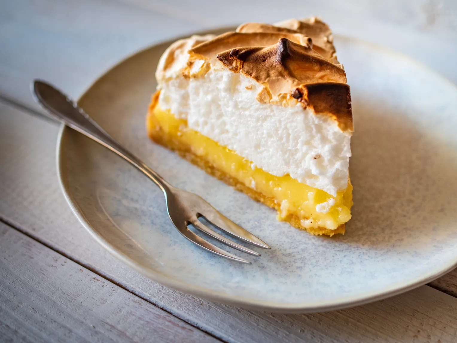 Ein Stück Zitronenkuchen auf einem Teller mit Kuchengabel auf einem Holztisch.
