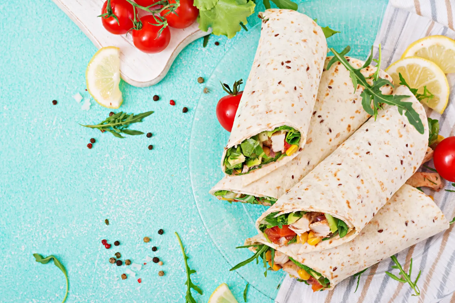 Burrito-Wraps mit Hühnchen und Gemüse auf hellem, türkisem Hintergrund.