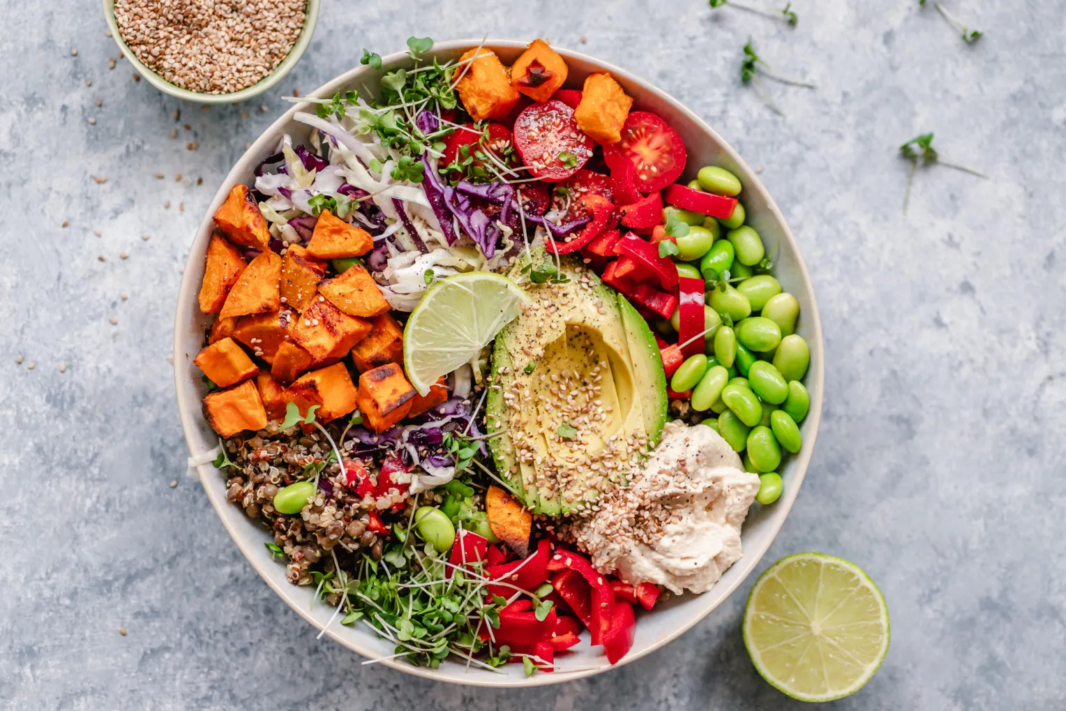 Draufsicht auf eine bunte vegane Bowl mit Quinoa, Süßkartoffel, Avocado, Hummus und einer Vielzahl von Gemüse.