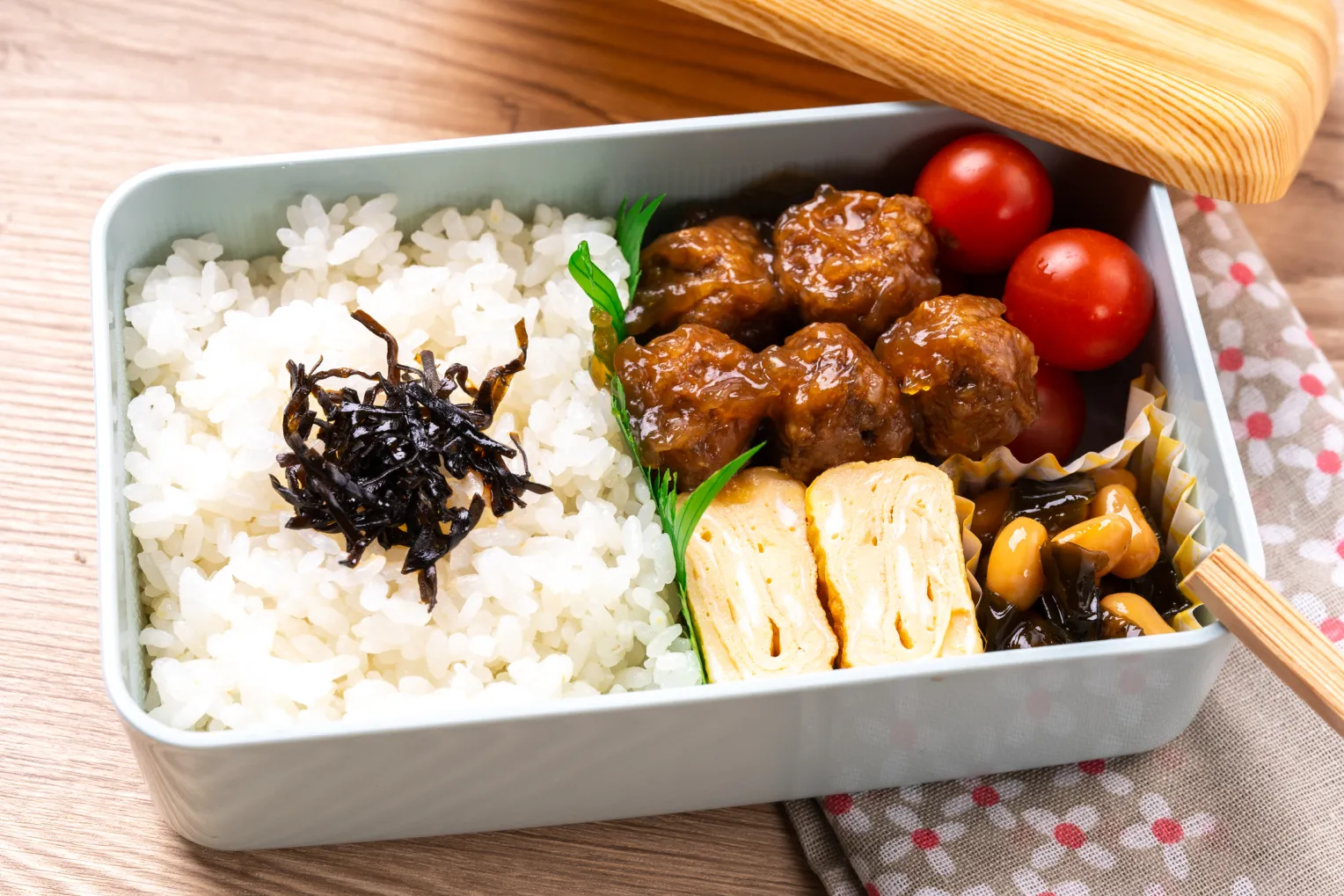 Fleischbällchen-Bento in einer geöffneten Lunchbox mit Holzdeckel auf einem Holztisch.
