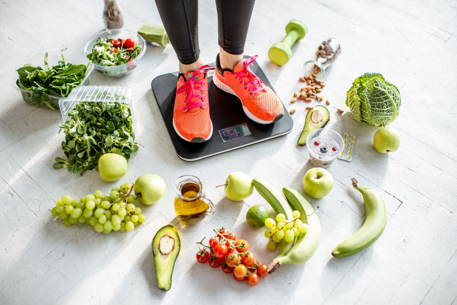 Eine Person in Sportkleidung steht auf einer digitalen Waage, umgeben von gesunden Lebensmitteln wie grünem Gemüse, Obst, Nüssen und Olivenöl. Die Szene vermittelt ein Bewusstsein für Ernährung und Fitness.