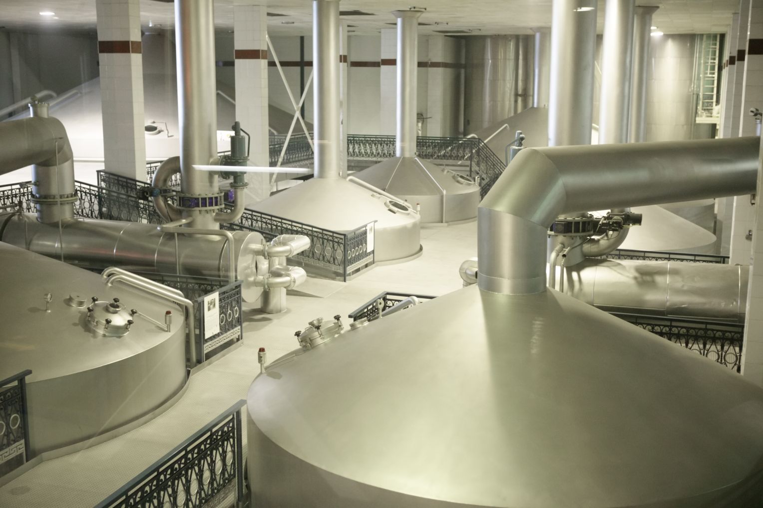 Innenansicht einer modernen Getränkefabrik oder Brauerei mit großen Edelstahlbehältern, Rohrleitungen und industrieller Ausstattung.
