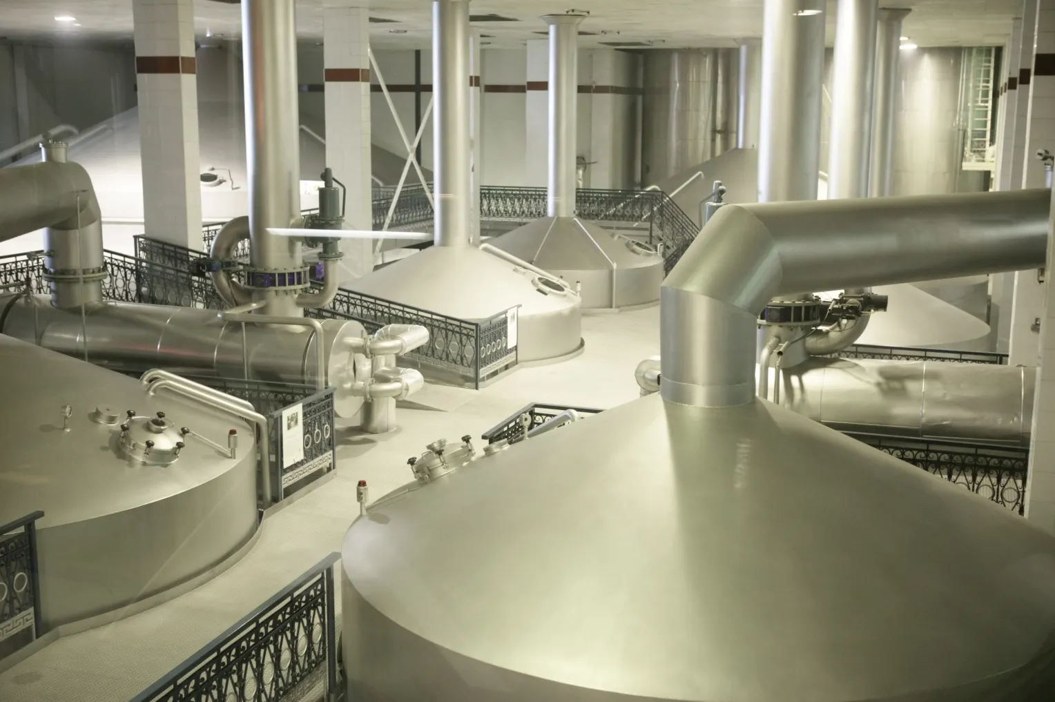 Innenansicht einer modernen Getränkefabrik oder Brauerei mit großen Edelstahlbehältern, Rohrleitungen und industrieller Ausstattung.