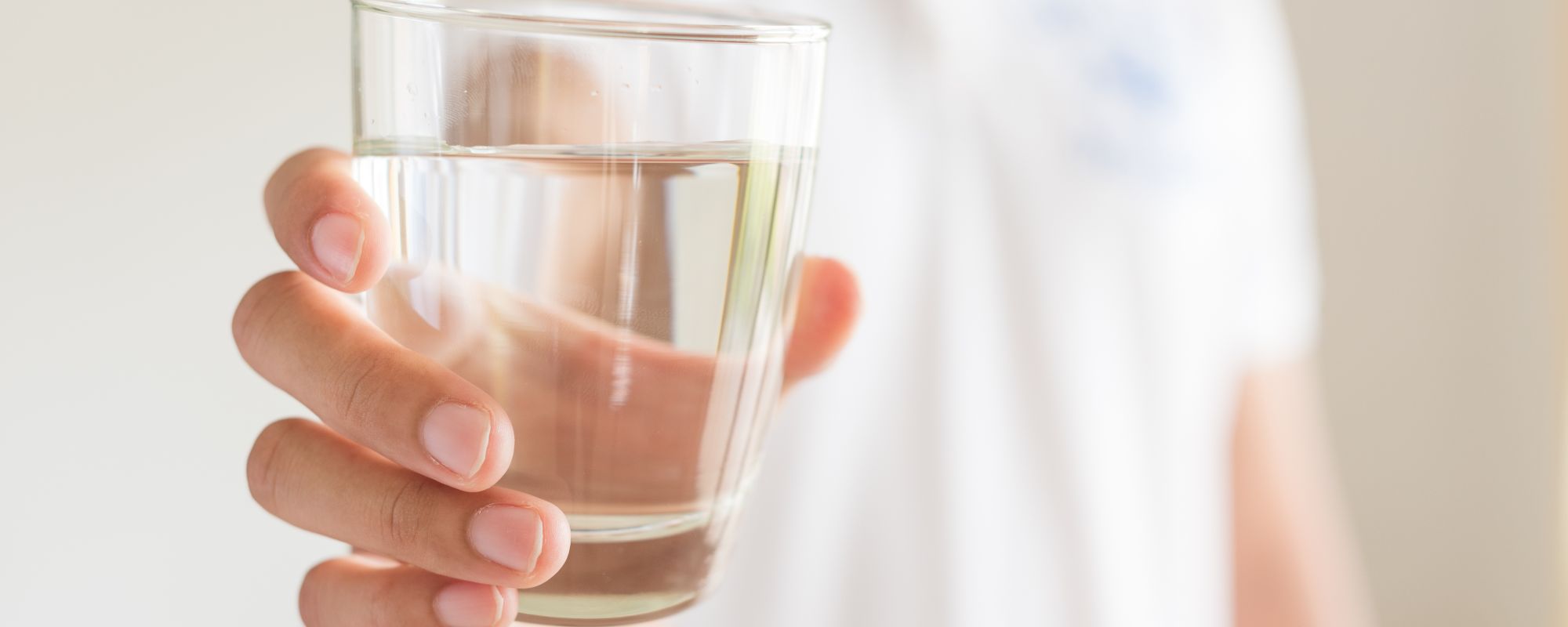 Eine Person in einem weißen Hemd hält ein Glas mit klarem Wasser in der ausgestreckten Hand.