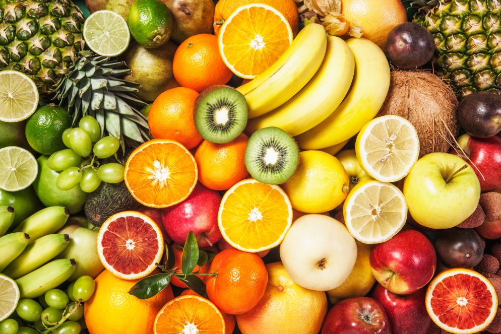 Vielfalt an frischem, farbenfrohem Obst wie Bananen, Orangen, Äpfel, Zitronen, Kiwis, Ananas und Trauben in einer Draufsicht.