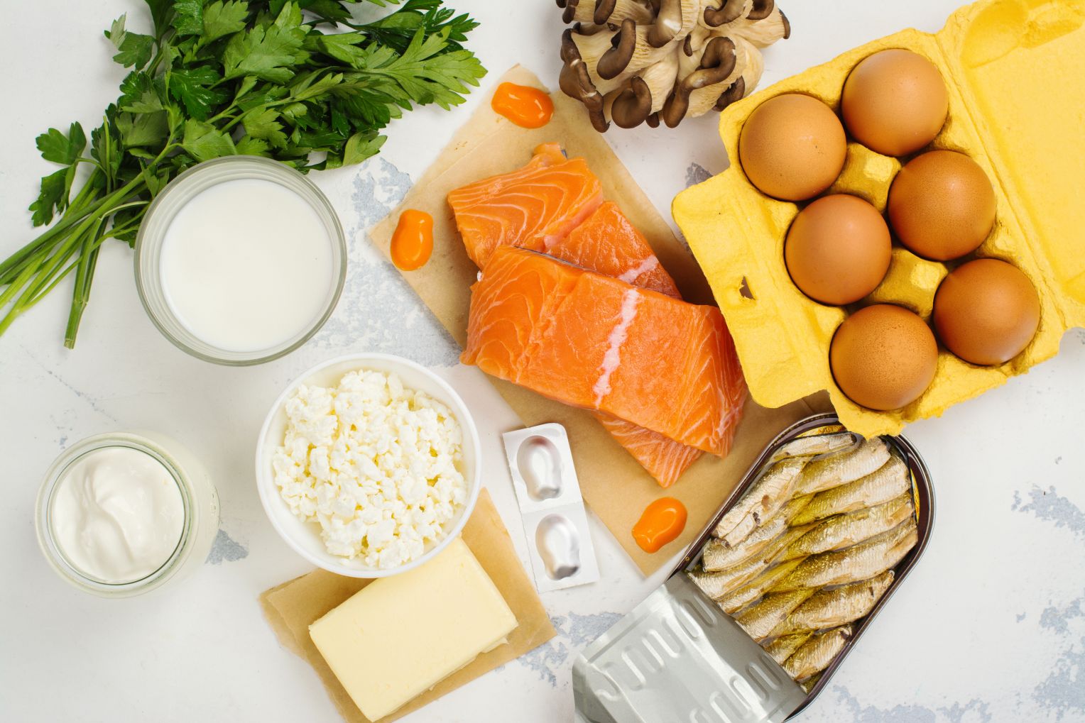 Lebensmittel mit hohem Vitamin-D-Gehalt: Lachs, Eier, Milchprodukte, Pilze, Dosenfisch und Nahrungsergänzungsmittel auf einem hellen Untergrund arrangiert.