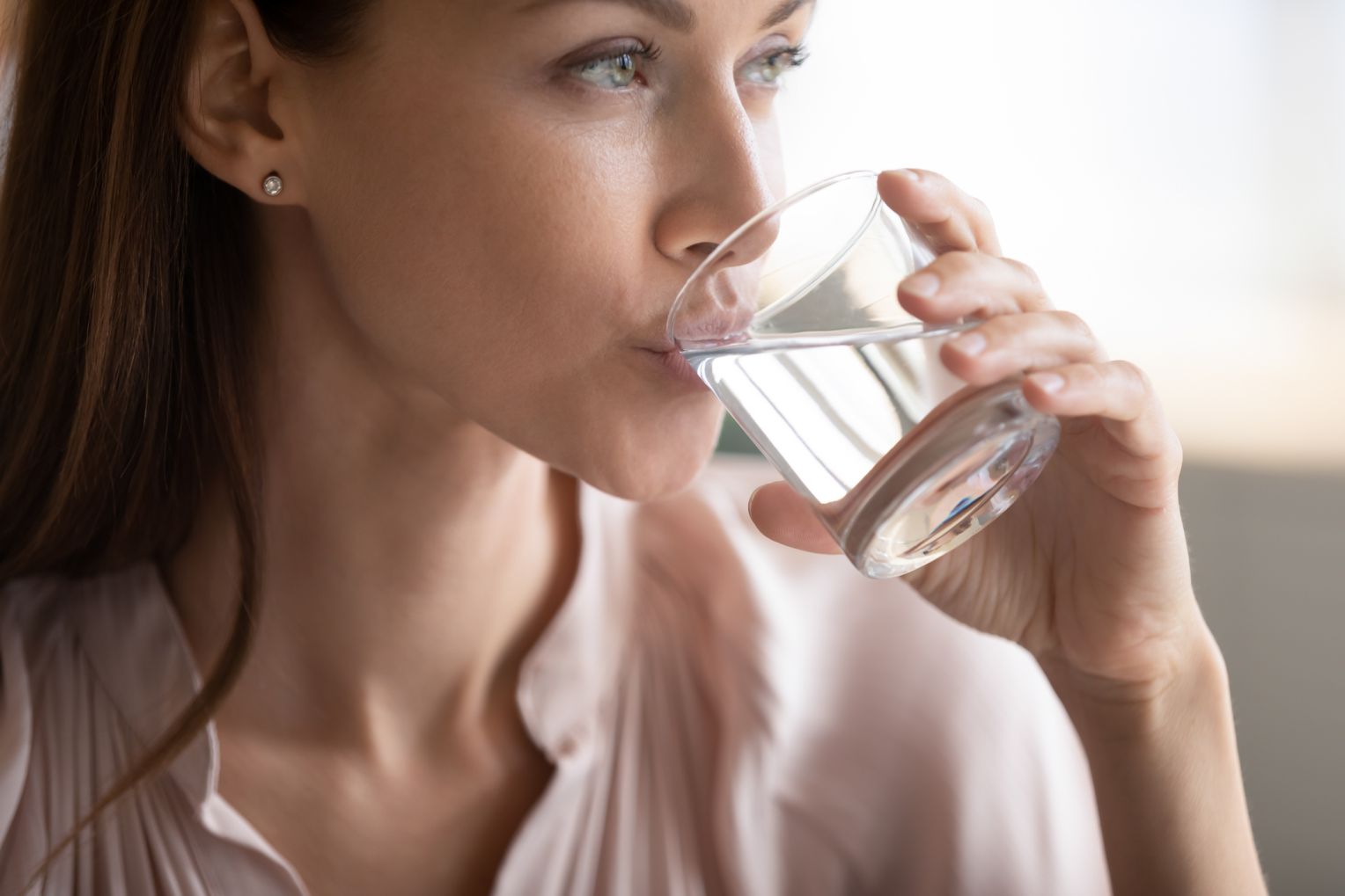 Frau trinkt ein Glas klares Wasser und schaut nach vorne.
