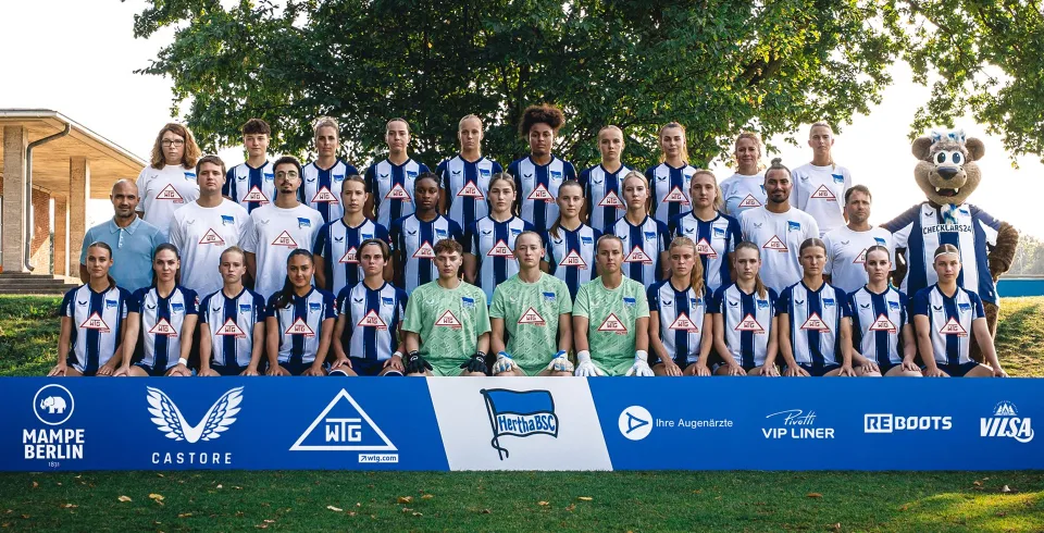 Frauenfußballmannschaft von Hertha BSC posiert mit Trainerteam und Maskottchen für ein offizielles Mannschaftsfoto; im Vordergrund stehen Sponsorenlogos, darunter VILSA.