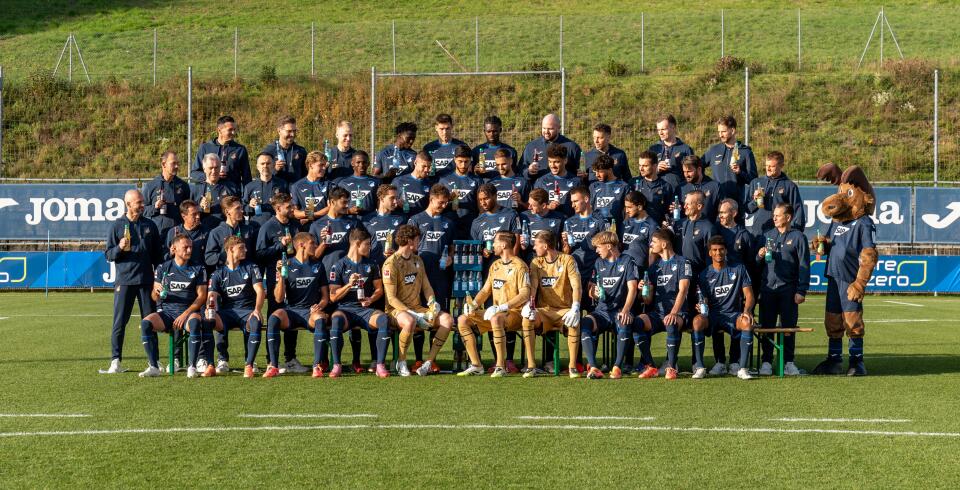 Fußballmannschaft und Betreuerteam posieren auf dem Trainingsplatz mit VILSA-Getränken und einem Maskottchen für ein Gruppenfoto.