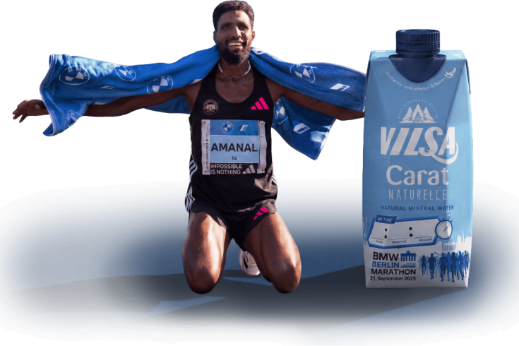Marathonläufer kniet nach dem Zieleinlauf mit Handtuch über den Schultern neben einer VILSA-Carat-Wasserpackung im BMW Berlin-Marathon-Design.