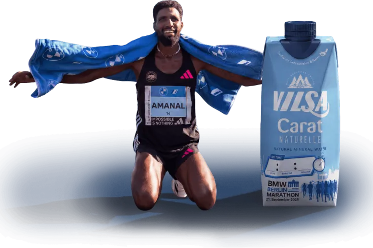Marathonläufer kniet nach dem Zieleinlauf mit Handtuch über den Schultern neben einer VILSA-Carat-Wasserpackung im BMW Berlin-Marathon-Design.