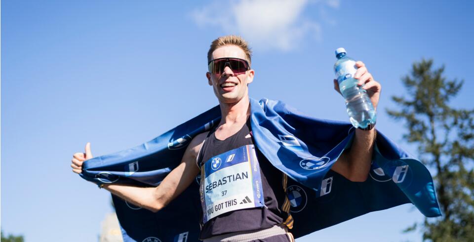 Marathonläufer mit Medaille hält eine Wasserflasche in der Hand und trägt ein blaues Handtuch über den Schultern.