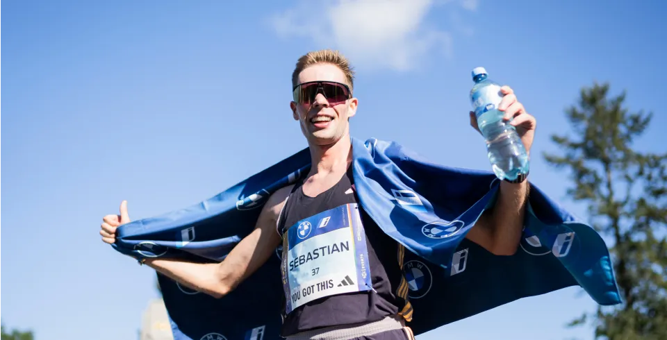 Marathonläufer mit Medaille hält eine Wasserflasche in der Hand und trägt ein blaues Handtuch über den Schultern.