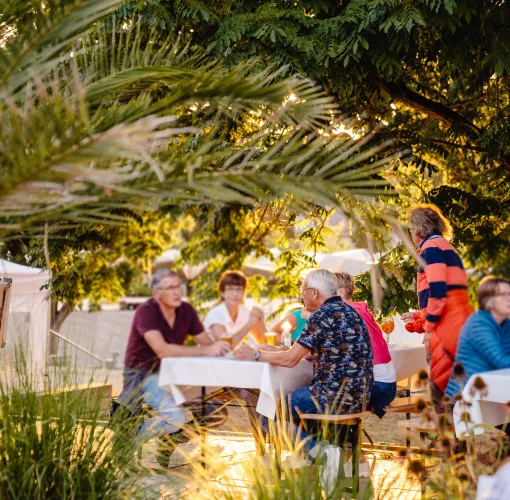 Gäste sitzen bei warmem Abendlicht an gedeckten Tischen im Grünen und genießen ein Outdoor-Gourmetfest.