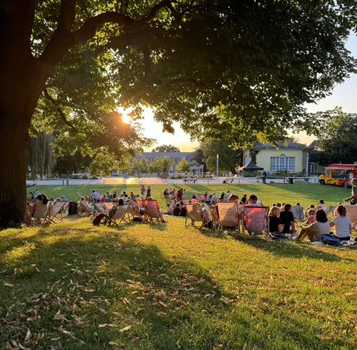 Menschen sitzen bei Sonnenuntergang in Liegestühlen auf einer Wiese im Kurpark Bad Nenndorf.