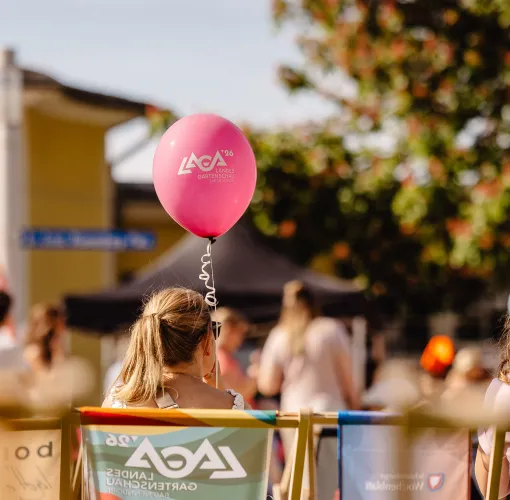 Personen sitzen in Liegestühlen bei einer Veranstaltung; ein pinker Ballon mit LaGa-Logo steht im Mittelpunkt.
