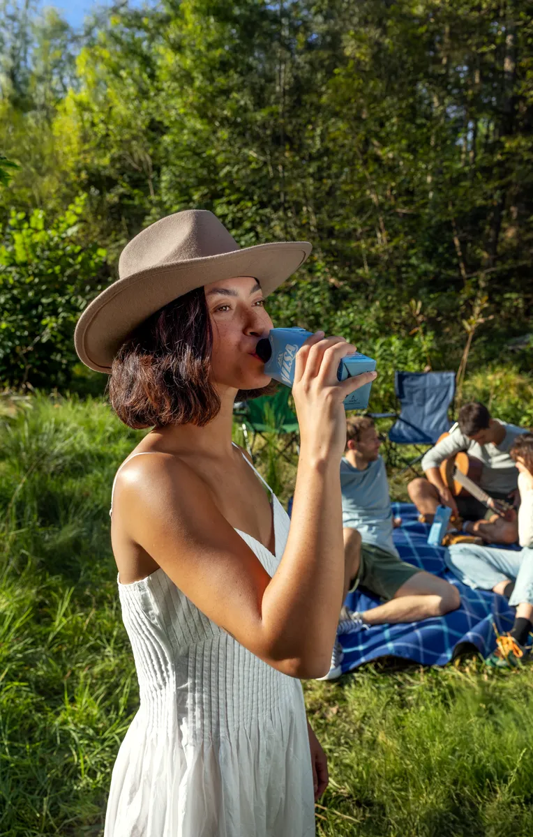 Junge braunhaarige Frau genießt Vilsa Carat Naturelle im Tetra Pak beim Picknick