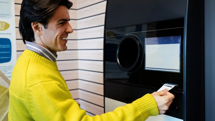 Mann steht an einem Pfandautomaten und hält eine ausgegebene Pfandquittung in der Hand.
