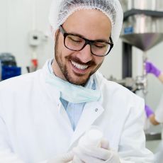 Mann im Laborkittel mit Brille lacht, auf der rechten Bildseite befindet sich das Institut Fresenius Logo