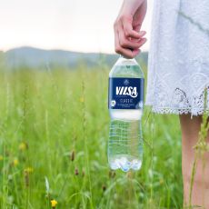 Frau mit weißem Kleid hält VILSA Mineralwasser classic rPET 1,0l in einem grünen Feld in der Hand