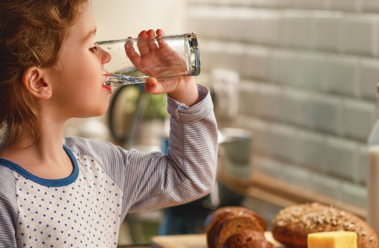 kleines Mädchen trinkt Wasser aus einem Glas in der Küche